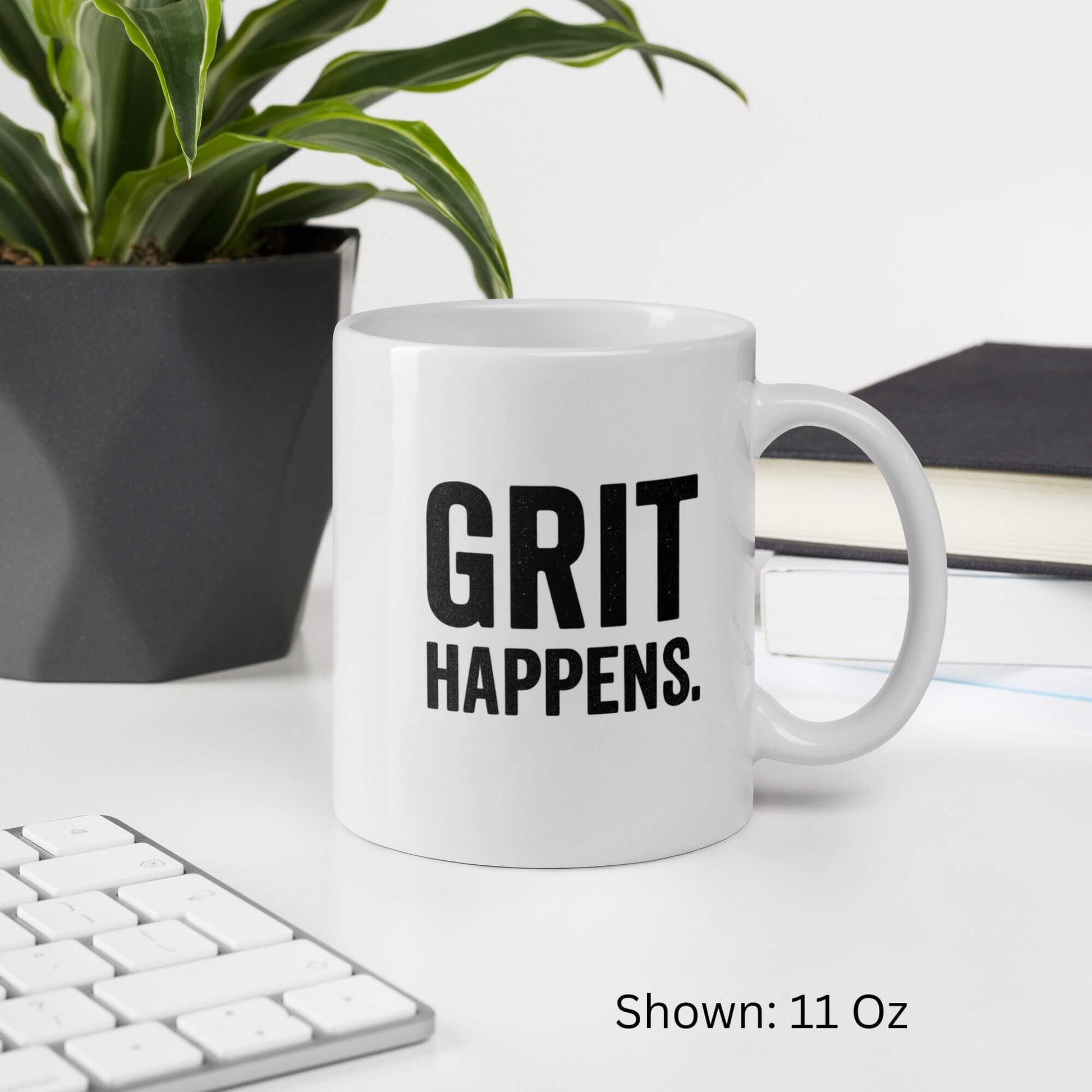 Mockup of the 11oz "Grit Happens" design on a white ceramic coffee mug by Grit Collective, shown on a desk.