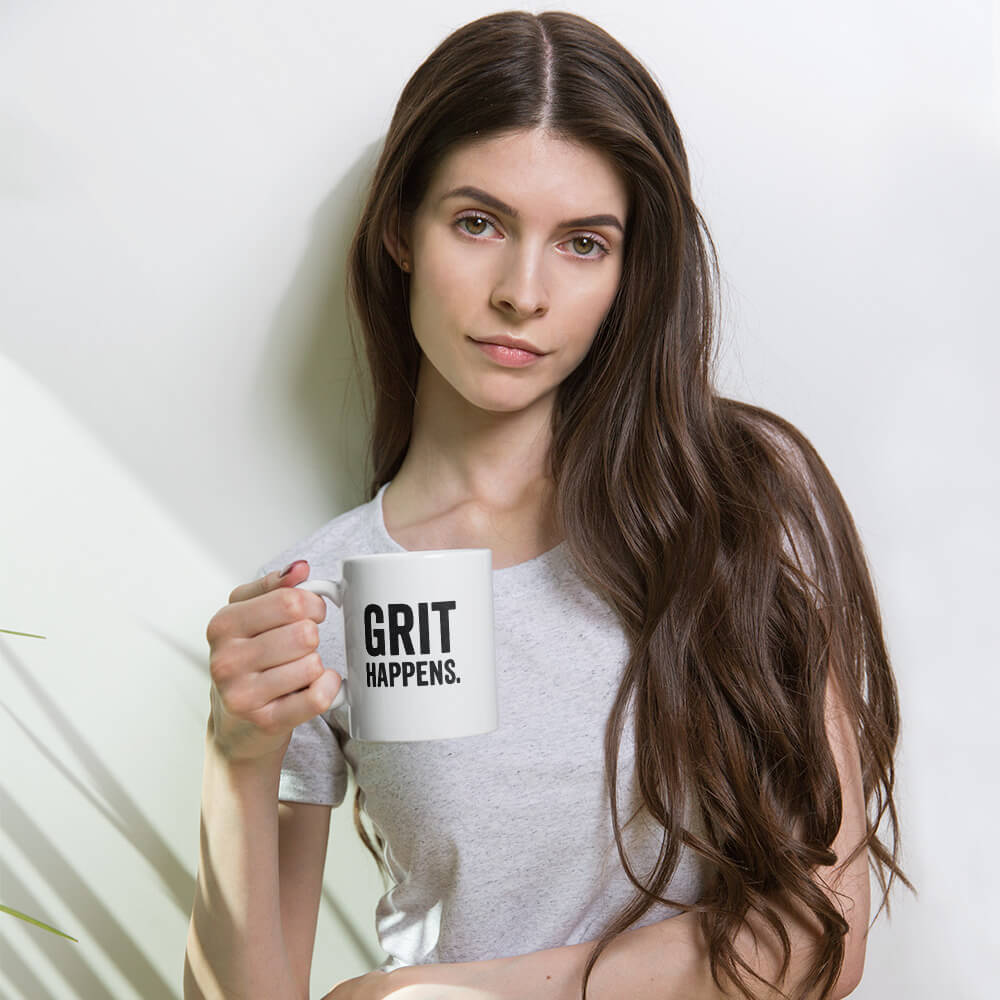 Woman holding the 11oz "Grit Happens" white glossy ceramic mug by Grit Collective.