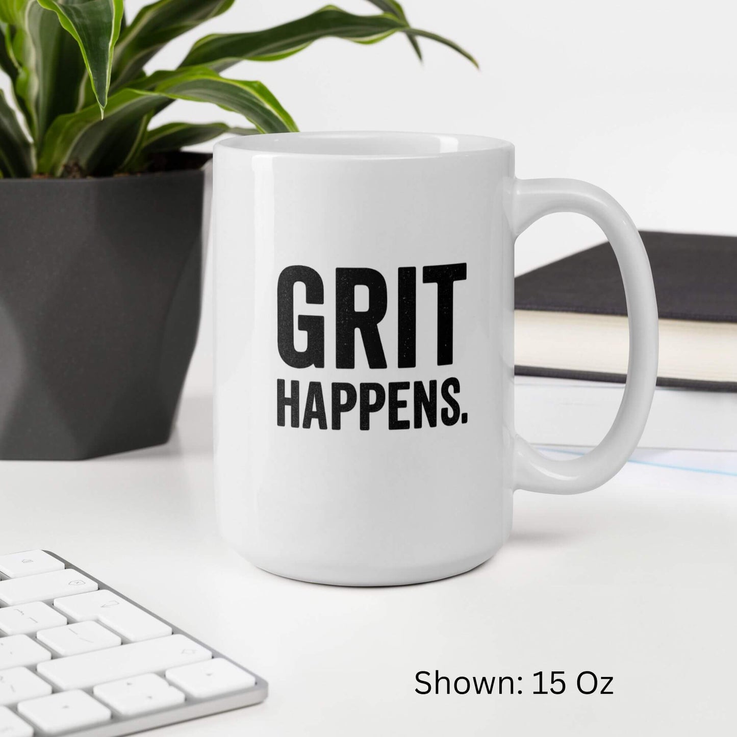 Mockup of the 15oz "Grit Happens" design on a white ceramic coffee mug by Grit Collective, shown on a desk.