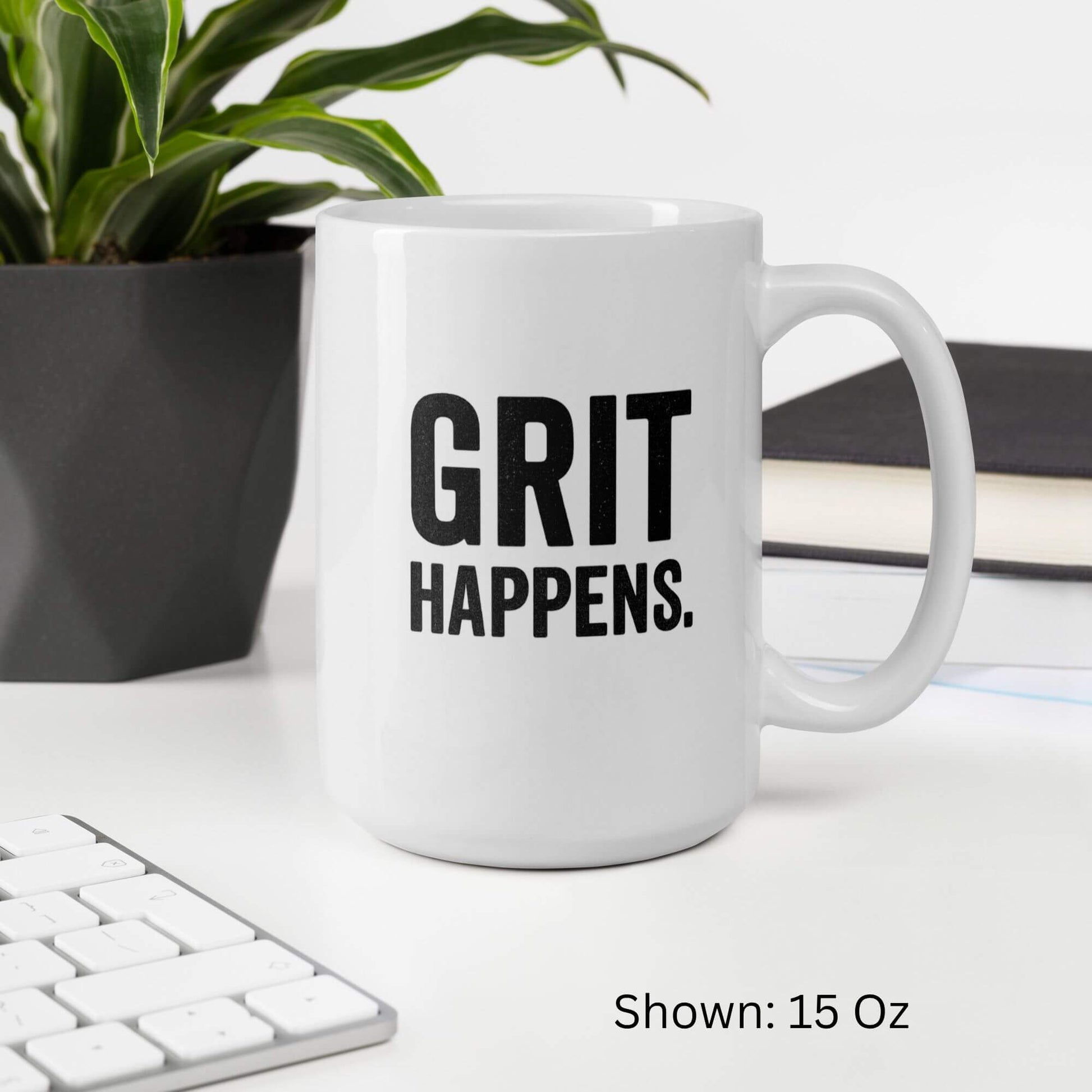 Mockup of the 15oz "Grit Happens" design on a white ceramic coffee mug by Grit Collective, shown on a desk.