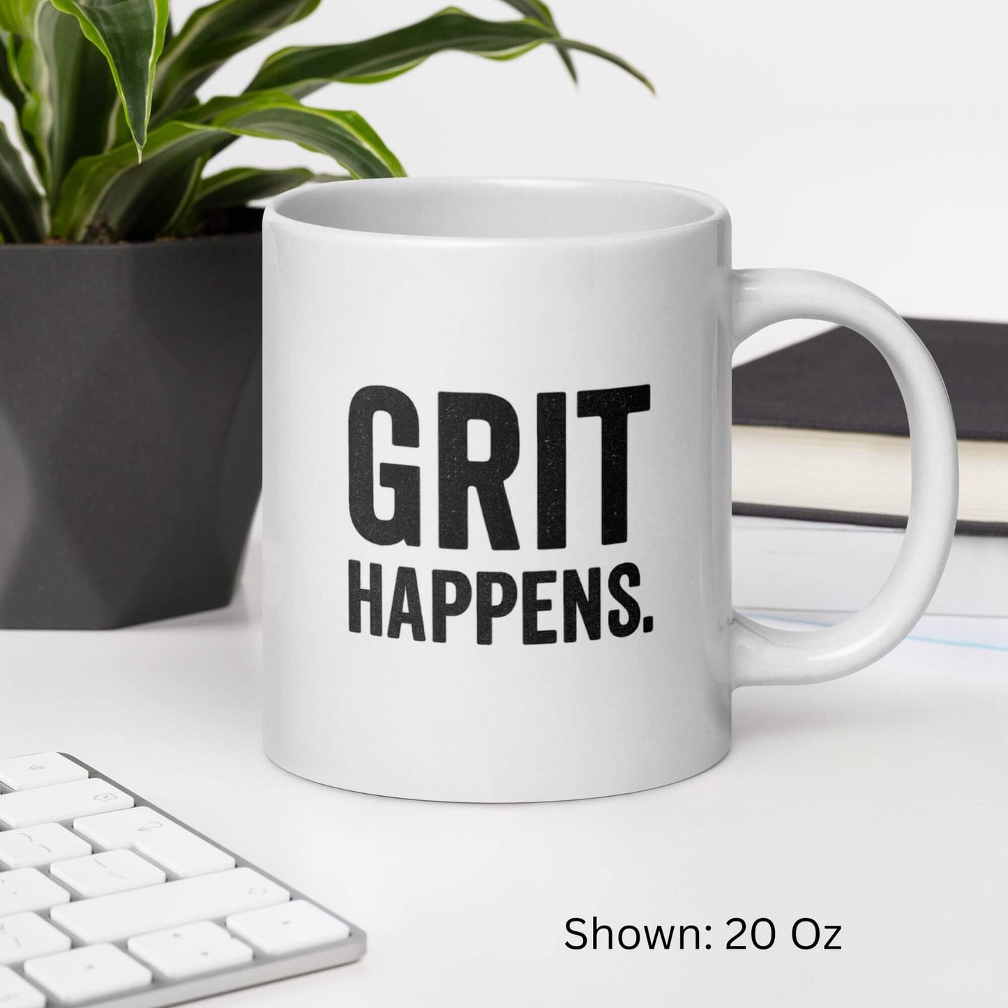Mockup of the 20oz "Grit Happens" design on a white ceramic coffee mug by Grit Collective, shown on a desk.