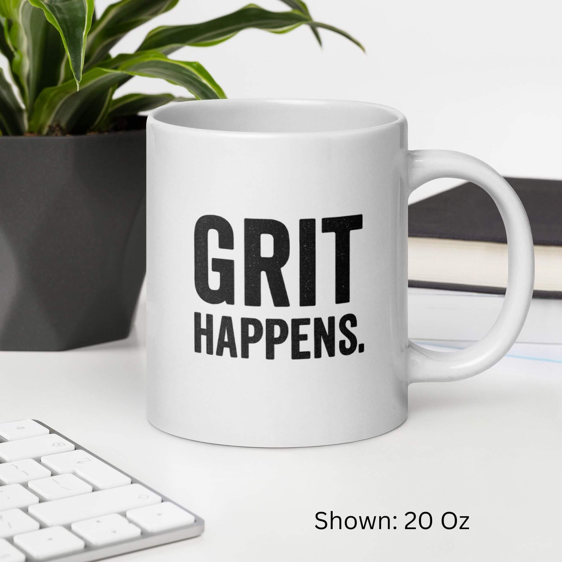 Mockup of the 20oz "Grit Happens" design on a white ceramic coffee mug by Grit Collective, shown on a desk.