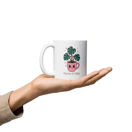 Grit Collective Kawaii Thriving Plant Pal design printed on an 11oz white glossy ceramic coffee mug, held in a hand.