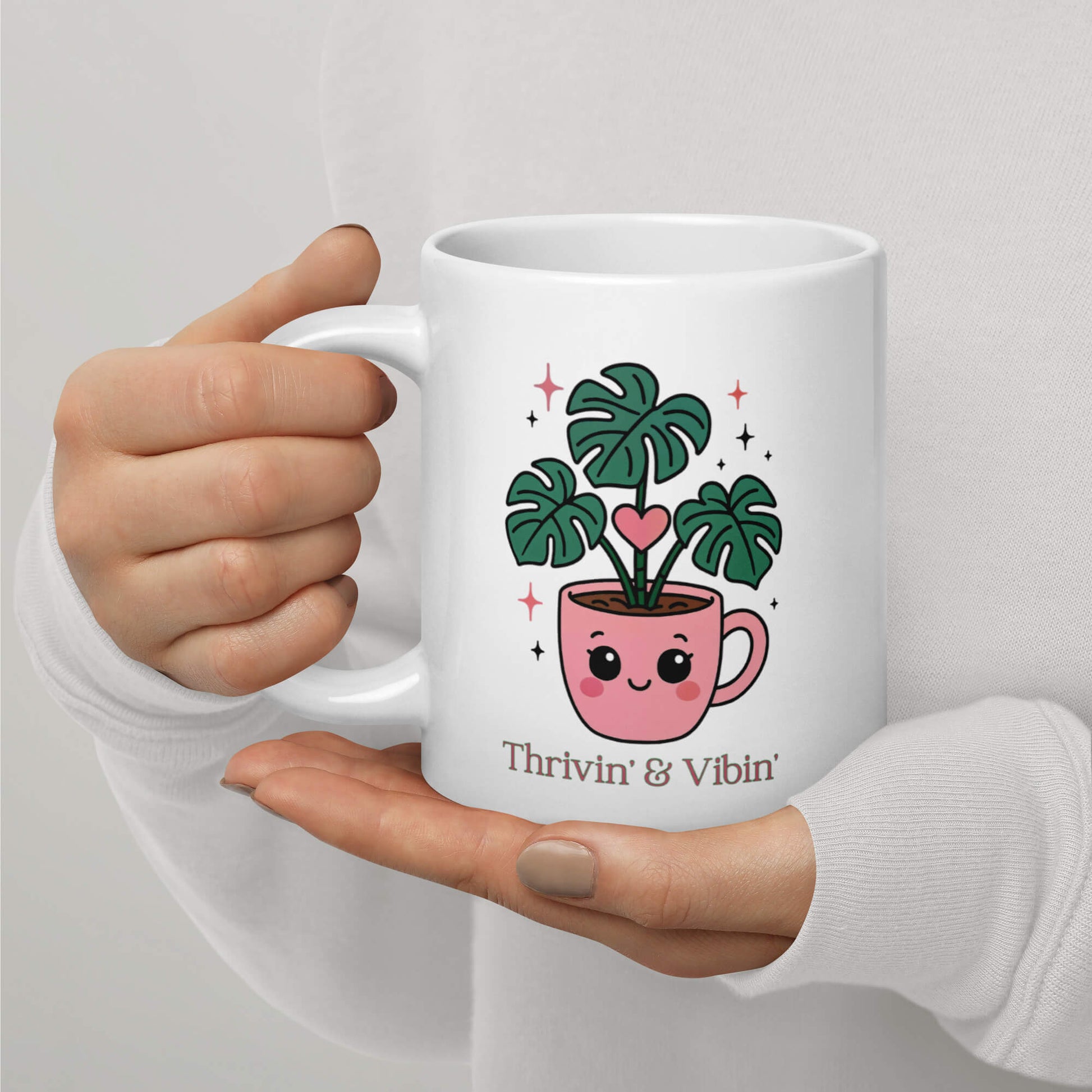Close up of hands holding a Grit Collective Kawaii Thriving Plant Pal design printed on a 20oz white glossy ceramic coffee mug.