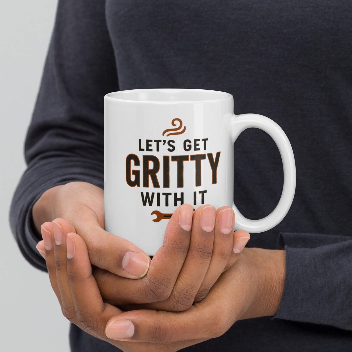 Close-up of the Grit Collective "Let's Get Gritty With It" wrench design on a white glossy ceramic coffee mug held in hands.