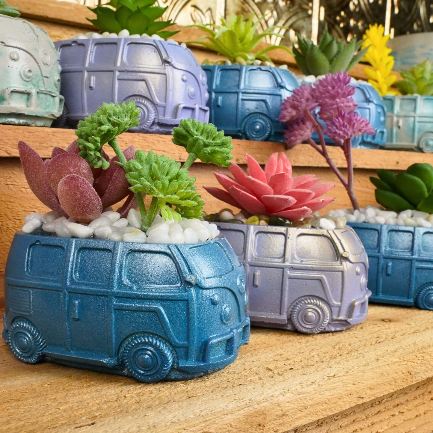 Assortment of handmade mini retro bus concrete planters in various metallic colors and with different artificial succulents, displayed on wooden steps.
