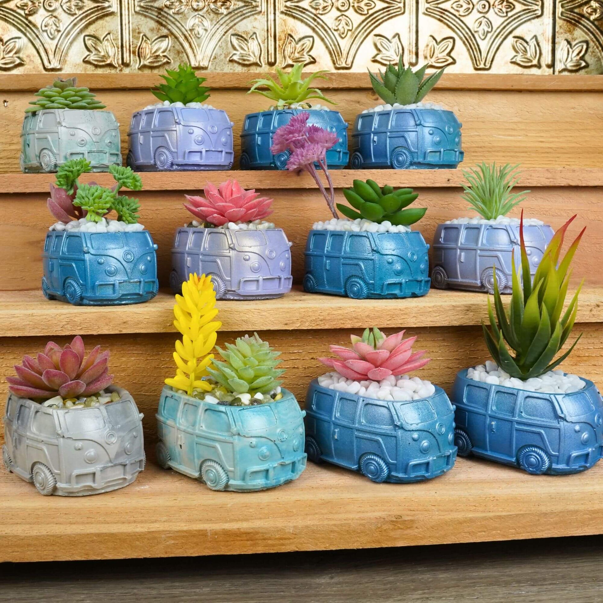 Large display of numerous handmade mini retro bus concrete planters in a variety of colors and with different artificial succulents, arranged on wooden steps.