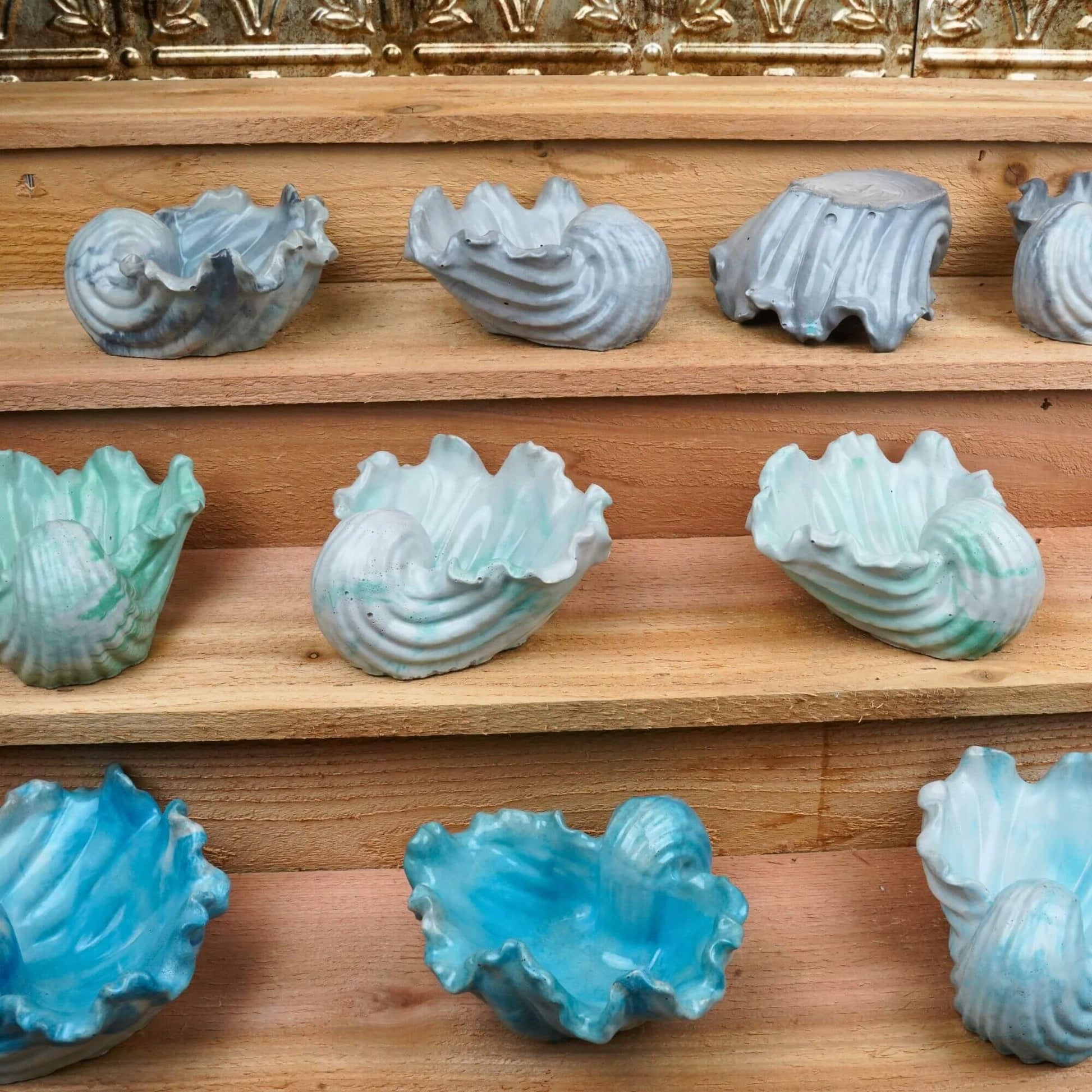 Collection of handcrafted concrete Ocean Bowls in various colors displayed on wooden shelves, showcasing the range of coastal charm dishes.