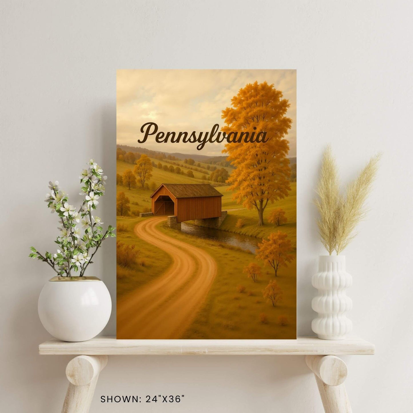 24"x36" canvas print featuring a scenic view of a covered bridge in a fall Pennsylvania setting,
displayed on a wooden shelf.