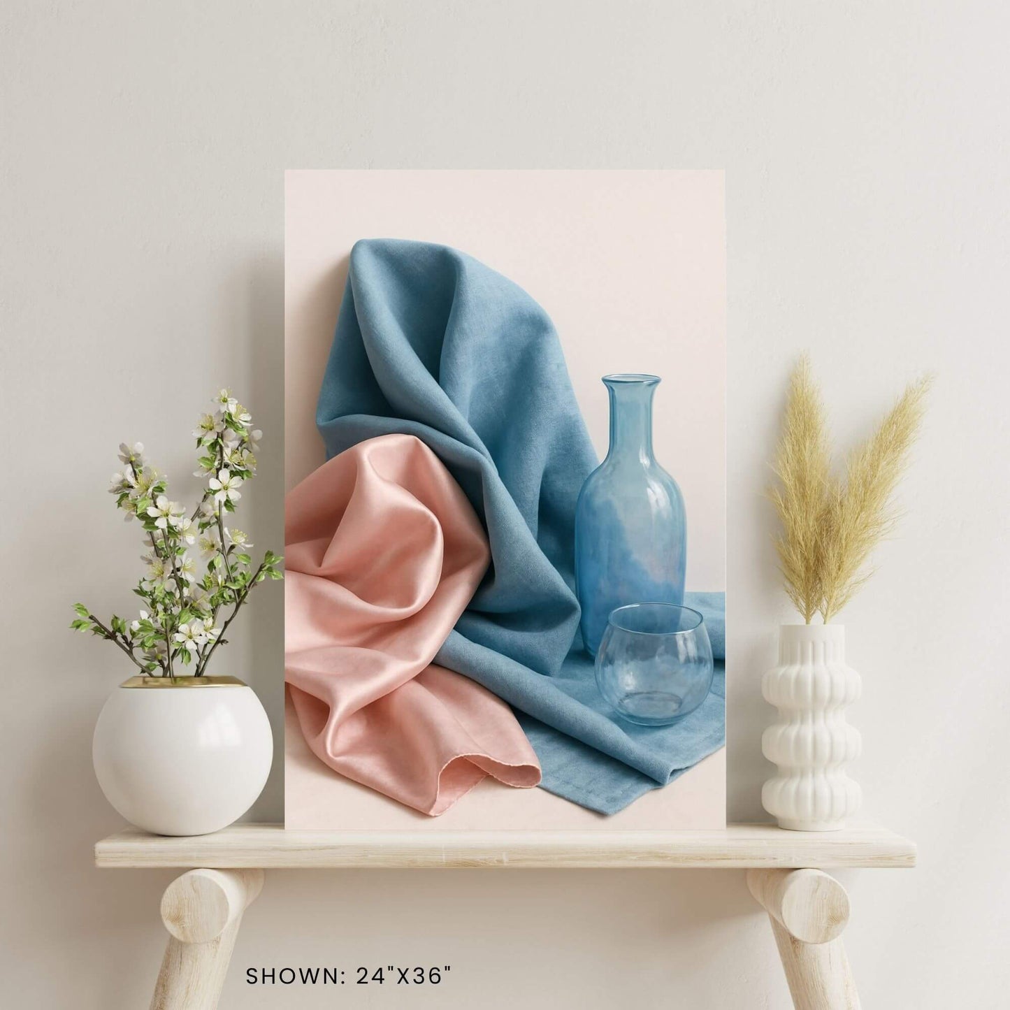 24"x36" canvas print featuring a still life of blue and pink fabric, a blue bottle, and a glass, shown on a decorative shelf.
