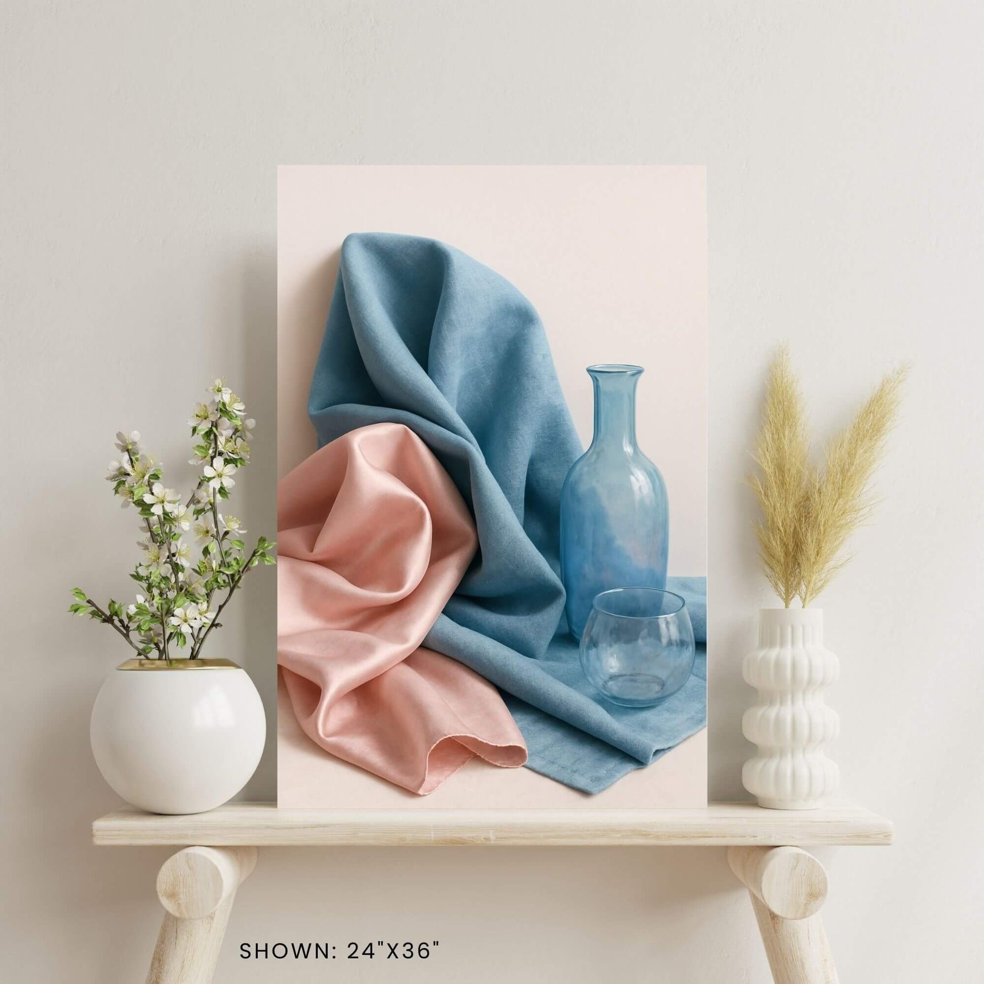 24"x36" canvas print featuring a still life of blue and pink fabric, a blue bottle, and a glass, shown on a decorative shelf.