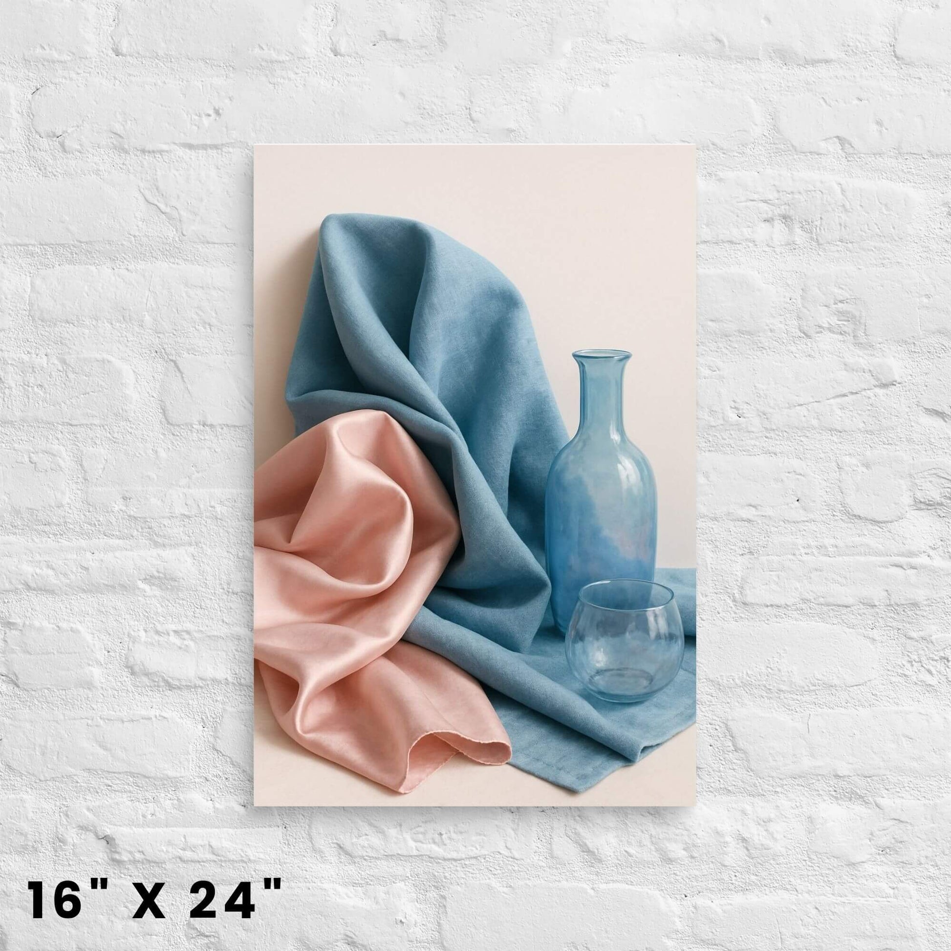 16"x24" canvas print featuring a still life with draped blue and pink fabric, a blue bottle, and a glass, displayed on a white brick wall.