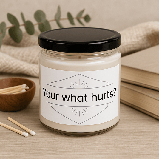 Your what hurts?" 9oz soy wax candle displayed with matches, books, and a small plant.
